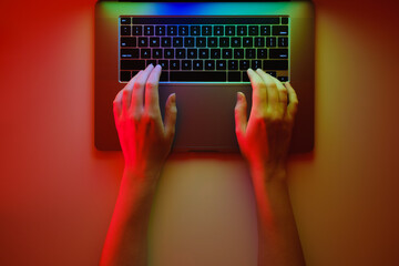 Hands on a modern laptop keyboard, top view and bright lit red b