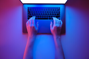 Hands on a modern laptop keyboard, top view in bright red and bl