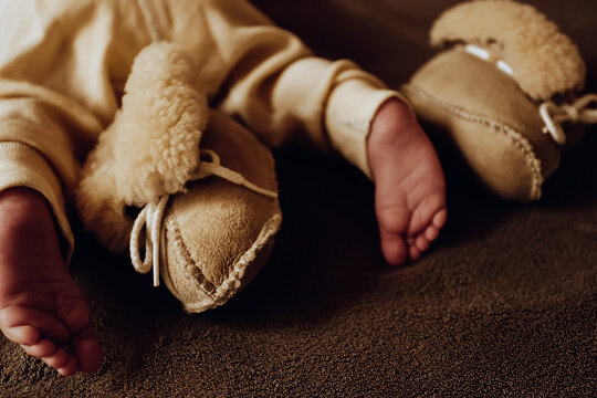 Toes of newborn baby with beige sheepskin booties and thermo pants