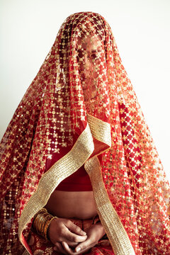 Indian bride looks out from under traditional red veil before wedding