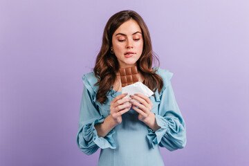 Portrait of funny brunette woman biting her lip in anticipation of tasty lunch. Girl in blue dress looks at delicious chocolate