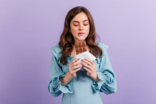 Portrait Of Funny Brunette Woman Biting Her Lip In Anticipation Of Tasty Lunch. Girl In Blue Dress Looks At Delicious Chocolate