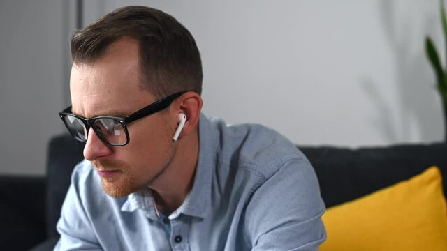 Close-up video portrair a pensive freelancer is thinking about solving business tasks. A smart young man in glasses using a laptop and lost in thoughts.