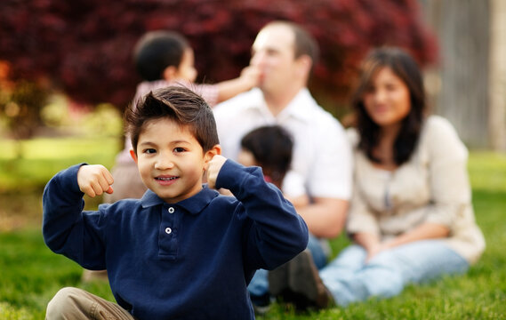 Boy flexing while sitting in front of family in grass