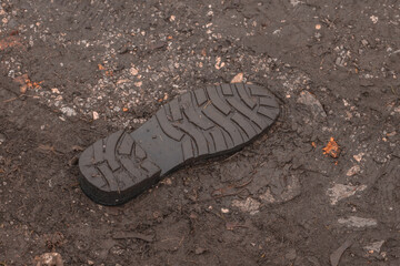 Underside of a shoe tread visible that it fell off and is now stuck in the mud.