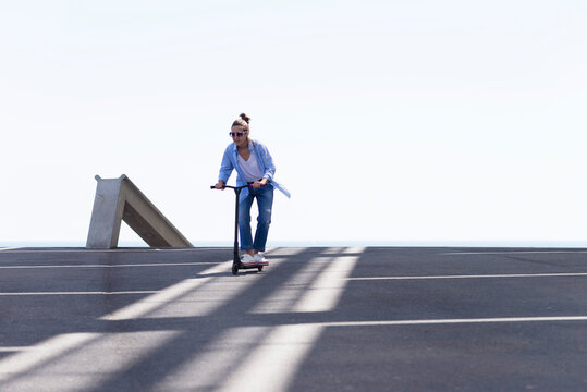 Woman with ponytail and sunglasses riding a scooter in the city