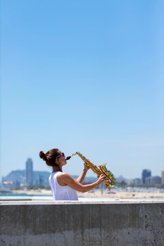 Woman with ponytail playing a saxophone while standing outdoors