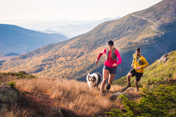 Man and woman trail running with dog in mountains at sunrise