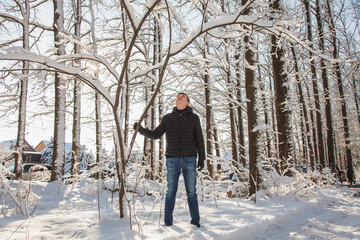 Fototapeta na wymiar Man shakes tree to make snowfall in winter snow-covered forest in sunny day