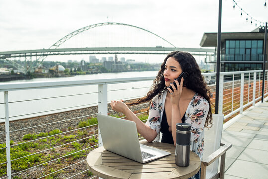 Woman sitting on rooftop with laptop talking on phone
