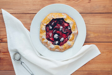 Delicious freshly baked vegan strawberry and cherry galette on wooden rustic background, top view. Sweet food, summer dessert.