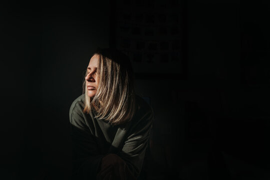 Blonde woman with dark background basking in the light with eyes close