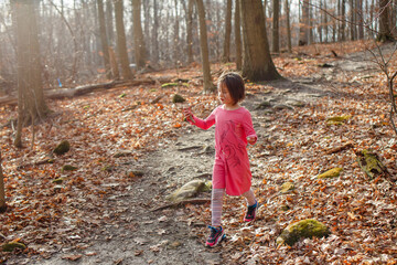 A little girl walks down a leafy path in autumn holding found treasure