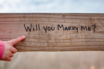 A child points out the words "Will you marry me?" written on a fence