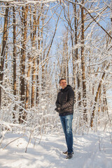 Man adjusts his glove in winter pine forest with snow on trees and floor in sunny day