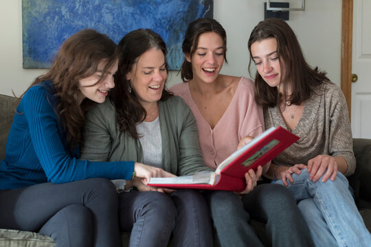 A mother and her three daughters laugh while looking at a photo album