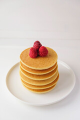 Freshly cooked soft delicious gluten free pancakes stacked on white plate, served with fresh raspberries, close up. Space for text. Healthy sweet food.