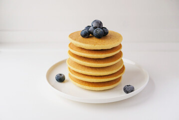 Freshly cooked soft delicious gluten free pancakes stacked on white plate, served with fresh bilberries, close up. Space for text. Healthy sweet food.