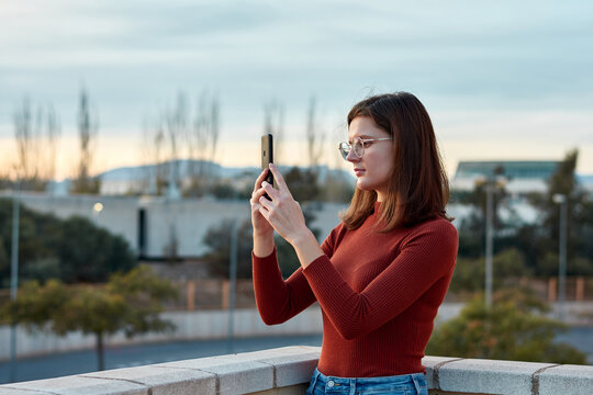Young woman is taking a photo with her mobile phone at sunset