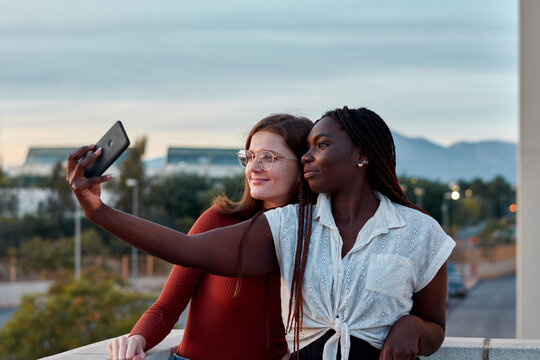 Two young women are taking a self-portrait with their phone at sunset