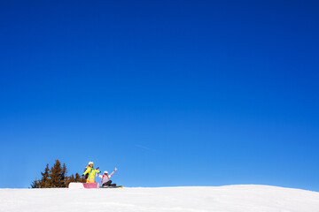 two female friends with ski and snowboard equipment posing on the snow.