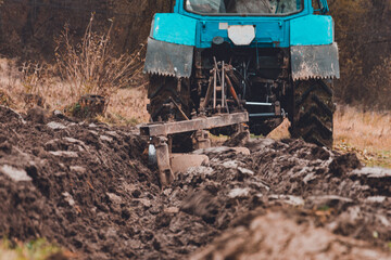 Land cultivation,tractor plows the ground, a blue small tractor and a plow with three knives.