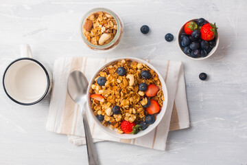 a bowl of cereal with mix berries, with a metal spoon and a jar of flakes