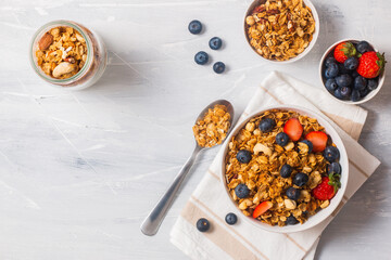 a bowl of cereal with mix berries, with a metal spoon and a jar of flakes