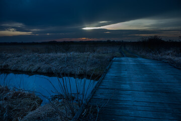 Wooden bridge on the river, sunset and dark evening sky