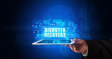 Young business person working on tablet and shows the digital sign: DISASTER RECOVERY