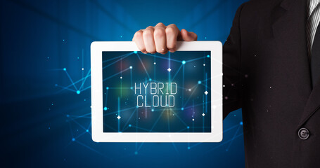 Young business person working on tablet and shows the digital sign: HYBRID CLOUD