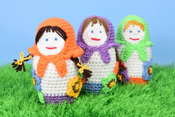 Crocheted dolls stand on green grass one after another
