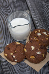 Oatmeal cookies with peanuts and chocolate. Nearby milk. On pine boards.