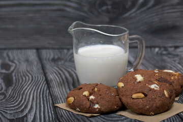 Oatmeal cookies with peanuts and chocolate. Nearby milk. On pine boards.