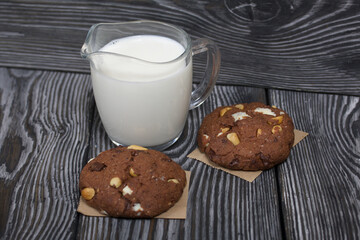 Oatmeal cookies with peanuts and chocolate. Nearby milk. On pine boards.