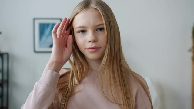 Slow motion portrait of cute teenage girl standing at home smiling touching hair and looking at camera. Adolescence and individuality concept.