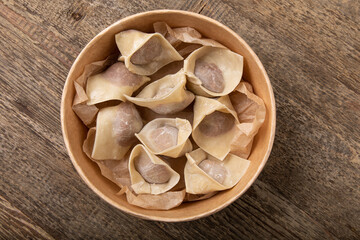 Uncooked dumplings in take away bowl on wooden table 