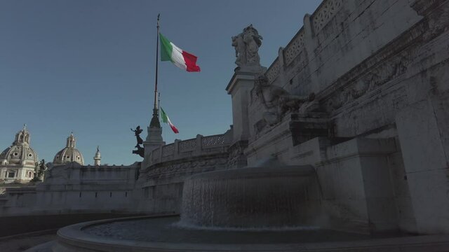 Rome, Italy - January 26, 2021: At Venice square in Rome  majestic monument of Vittorio Emanuele II called Vittoriano, low angle view show marble fountain and decoratives and italian flag in blue sky