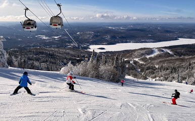 Skiers on Mont Tremblant slopes with aerial gondolas on the background, Quebec, Canada