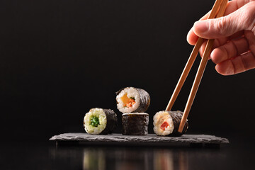 Hands picking vegetable maki sushi with chopsticks and black background