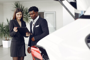 Man buying the car. Assistant helps to choose a car. Businessman in a car salon. Black male in a suit.