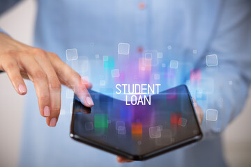 Young man holding a foldable smartphone with STUDENT LOAN inscription, educational concept
