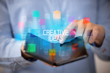 Young man holding a foldable smartphone with CREATIVE IDEAS inscription, educational concept