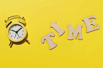 Home composition. Consists of a clock and the word "time" on a yellow background. Flat lay, top view, copy space.