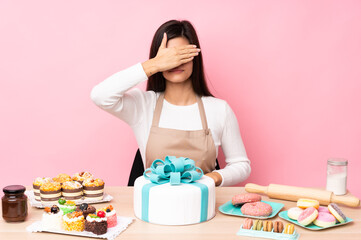 Obraz na płótnie Canvas Pastry chef with a big cake in a table over isolated pink background covering eyes by hands. Do not want to see something