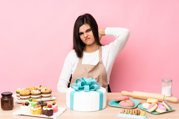 Pastry chef with a big cake in a table over isolated pink background with neckache