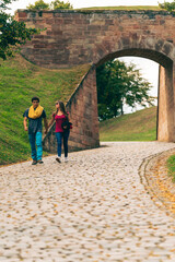 Young couple walk hand in hand on a cobbled path in a historic site.