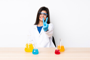 Young scientific woman in a table smiling and showing victory sign