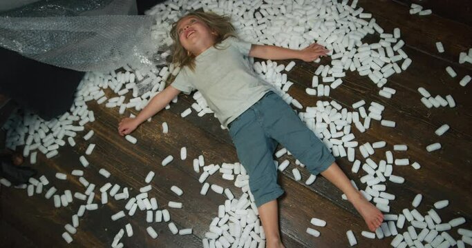 A preschooler is making snow angels with styrofoam balls on the floor at home