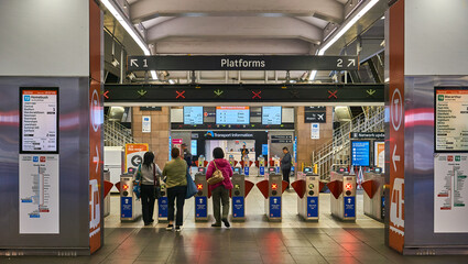 Naklejka premium Metro, tube, subway, railway entrance to station. Commuters sliding card to enter. Stairs leading to platforms. Guide signs, lights and turnstiles. Sydney, NSW.